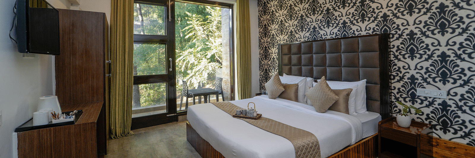 The deluxe room at DLS Whispering Winds featuring a bed, bed side tables, flat screen TV, other room amenities and a glass door leading to the balcony